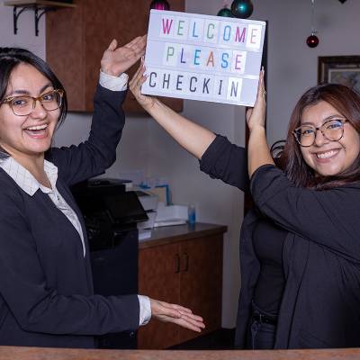 Front desk team holding a Welcome Please Check In sign